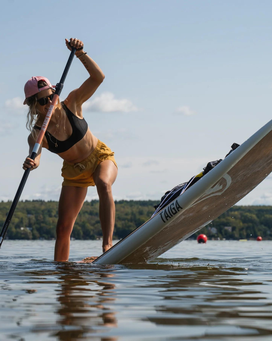 Woman paddleboarding on the Hana 9'5" on a lake with trees and clear sky in the background 