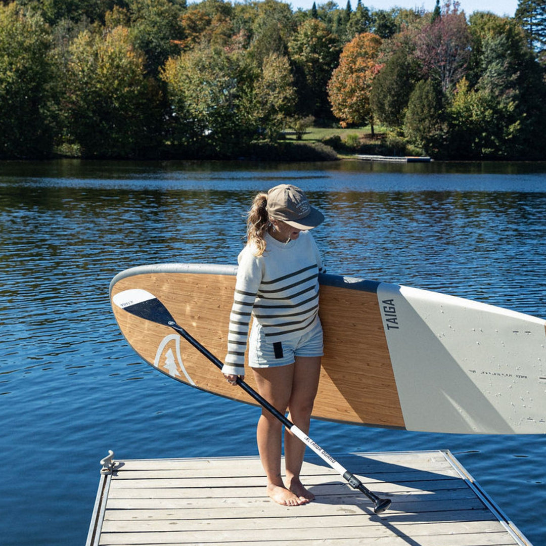 Woman with a paddle and a Taiga stand-up paddleboard on a dock by a lake.
