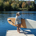 Woman with a paddle and a Taiga stand-up paddleboard on a dock by a lake.