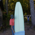 Person holding a sage surfboard with a forest background