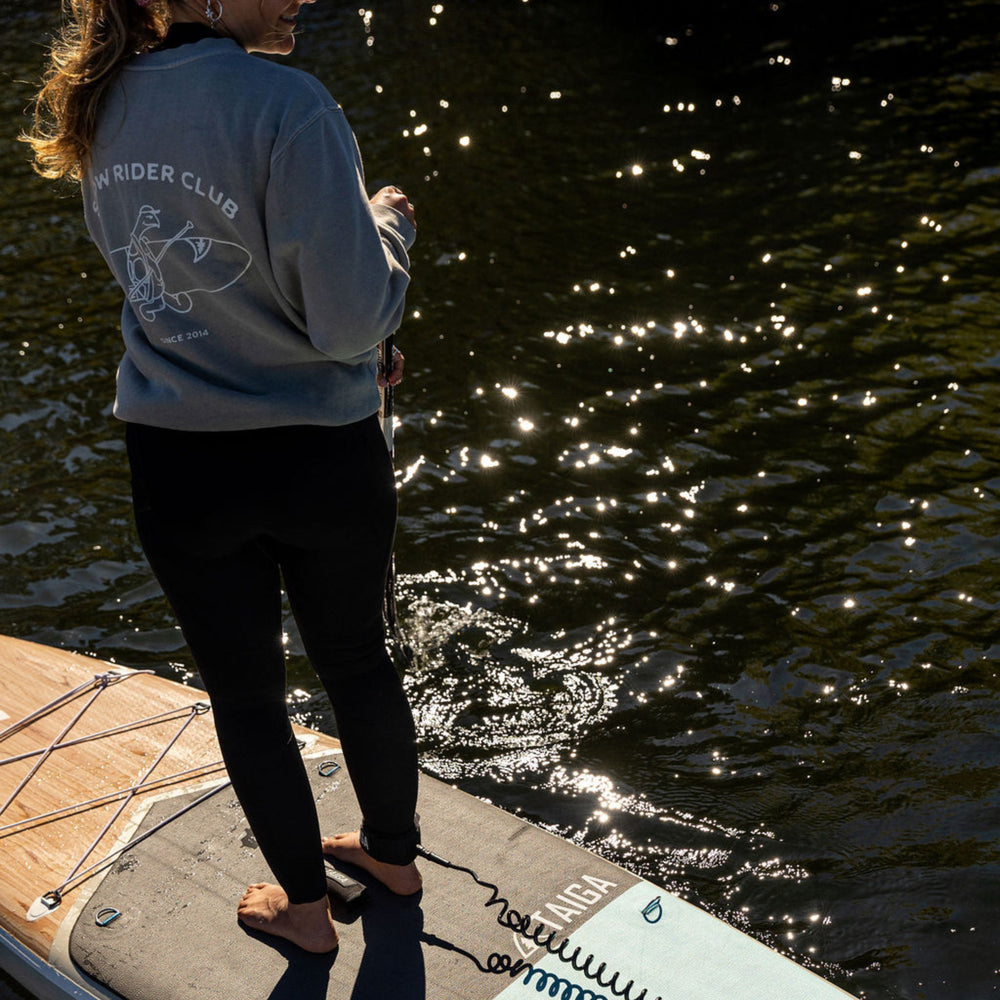 Person standing on a paddleboard, wearing a crewneck with 'Slow Rider Club' text.