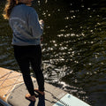 Person standing on a paddleboard, wearing a crewneck with 'Slow Rider Club' text.