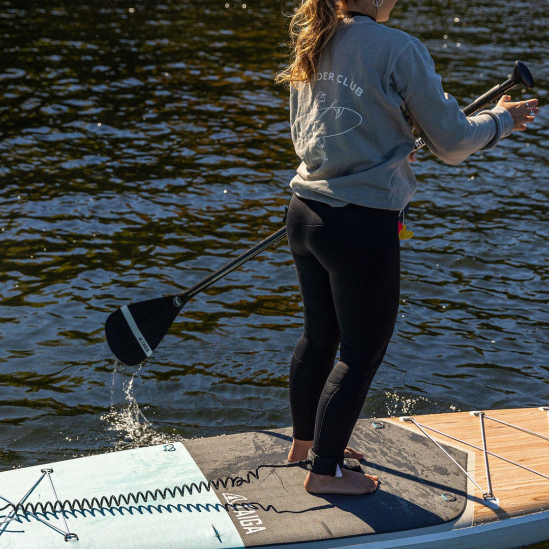 Person standing on a paddleboard, wearing a crewneck with 'Slow Rider Club' text.
