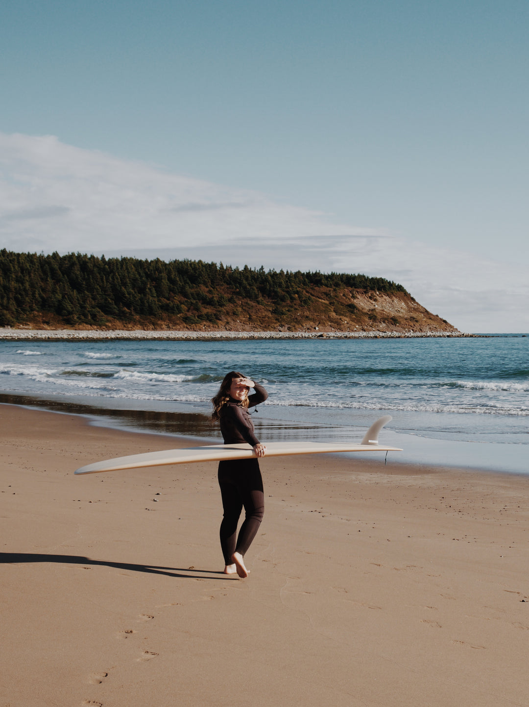 Person walking on a beach with a surfboard, surrounded by ocean.