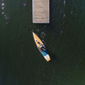 Aerial view of a person paddling a SUP near a wooden dock on a lake.