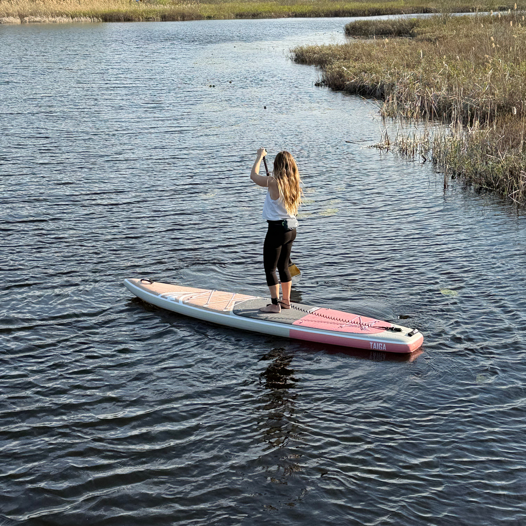 Person standing on a paddleboard in a body of water with reeds in the background