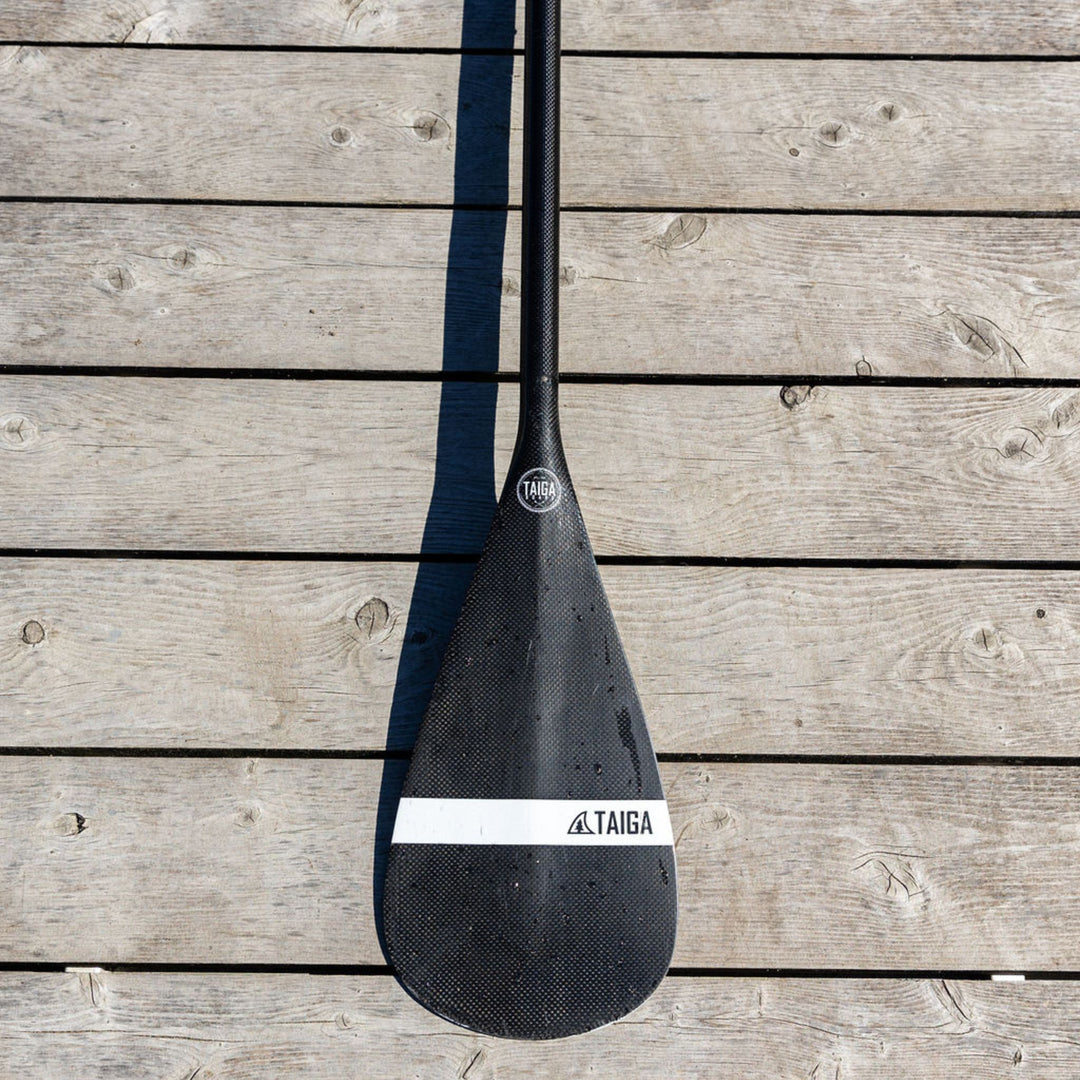 Black paddle on a wooden surface, featuring the Taiga brand.