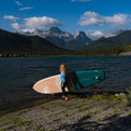 Person holding a paddleboard by a lake with mountains in the background