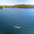 Person paddleboarding on a calm lake with trees and mountains in the background