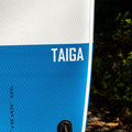 Blue and white paddleboard with 'TAIGA' branding against a natural background