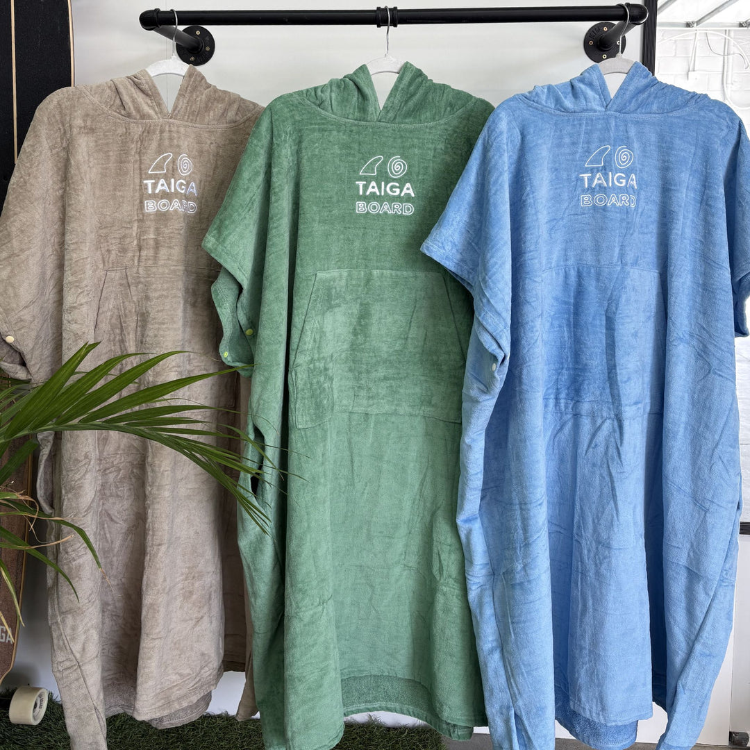 Three hooded towels in brown, green, and blue hanging on a rack with 'TAIGA BOARD' branding.