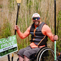 Man in a wheelchair holding a paddle with reeds and a sign in the background