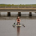Two people on an Adaptive Inflatable Paddle Board with stabilizers in calm water.
