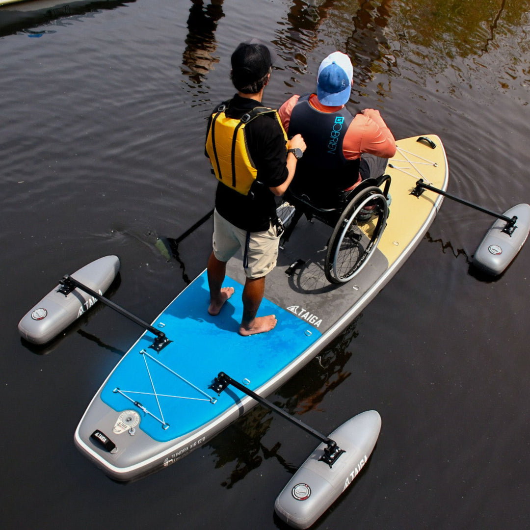 Two people on an Adaptive Inflatable Paddle Board with stabilizers in calm water.