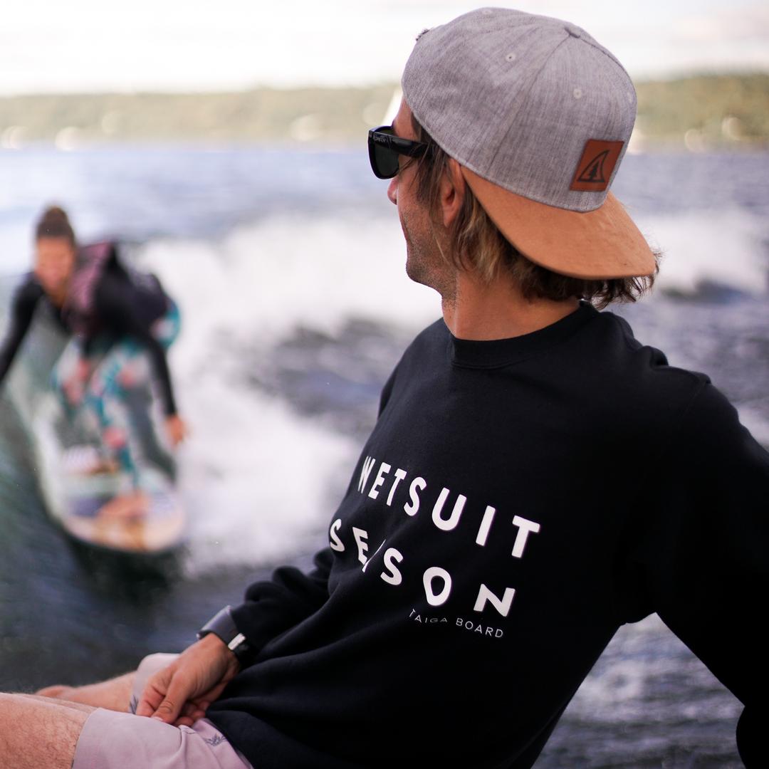 Surfer wearing the black WETSUIT SEASON Crewneck by TAIGA BOARD